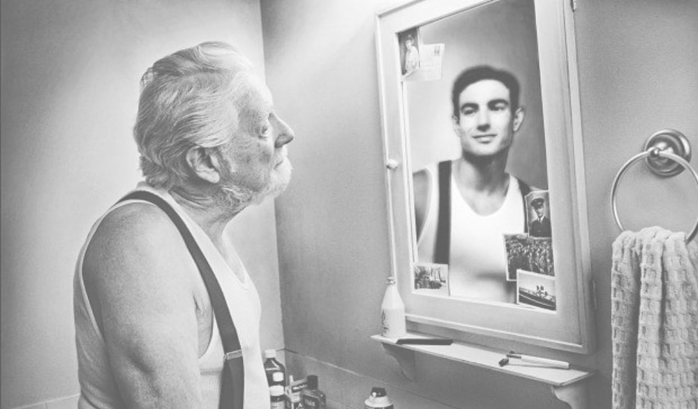 old man looking into mirror of young self